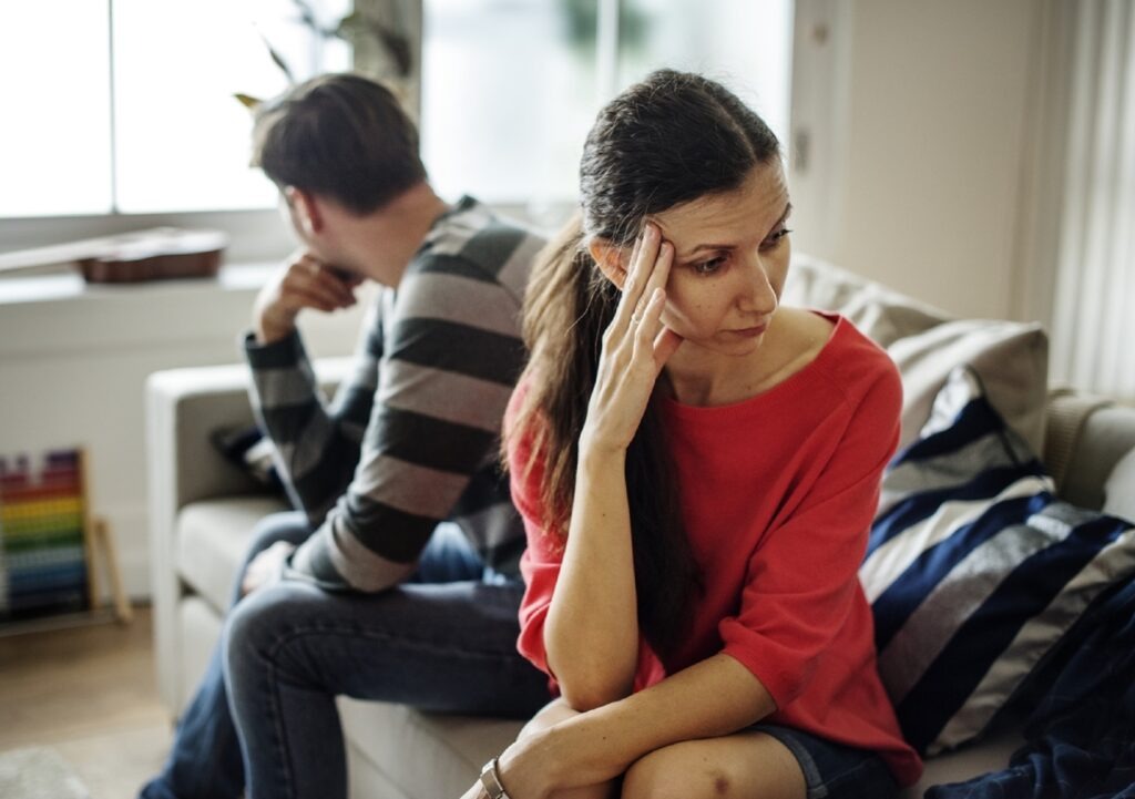 Couple sitting on couch far apart from each other.